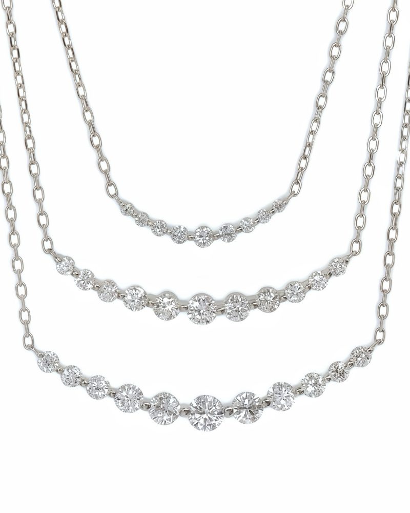 Three K white gold gradient smile diamond necklaces displayed in layered rows, each set with a curved bar of gradient round brilliant diamonds, shown against a white background. K白金漸層微笑排鑽項鍊展示圖，呈現三條不同尺寸、呈弧形排列的漸變圓形明亮式鑽石項鍊，背景為純白色。