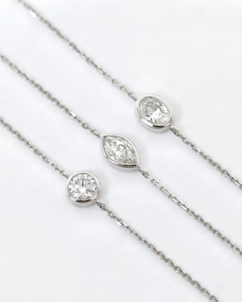 Three white gold fine chain bracelets featuring bezel-set diamonds in round, marquise, and oval cuts displayed side by side against a white background. 三條白金細鍊手鍊並排展示，分別採用包鑲（Bezel setting）工藝呈現圓形、欖尖形與橢圓形切割鑽石，背景為純白色。