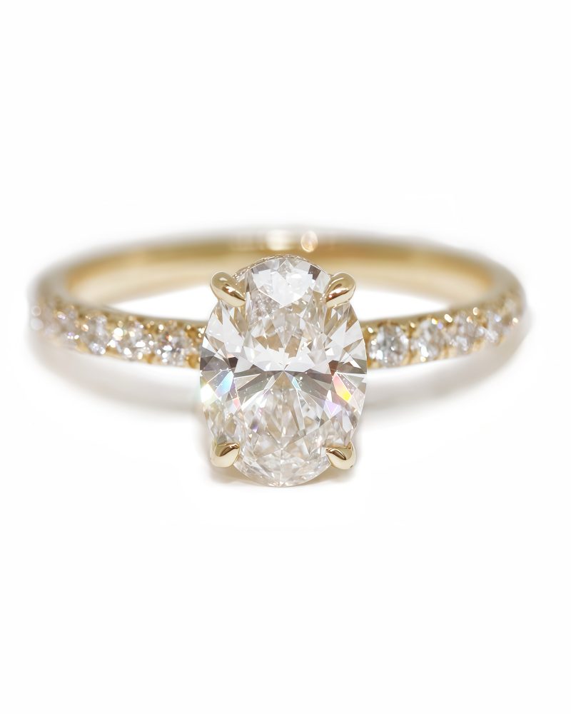Front view of a yellow gold promise ring featuring a central oval-cut diamond in a four-prong setting with a pavé diamond band and hidden halo against a solid white background. 黃金求婚戒指正面圖，展示中央四爪鑲嵌的橢圓形切割鑽石，以及密鑲鑽石戒身（Pavé band）並有隱藏鑽石圍鑲，背景為純白色。