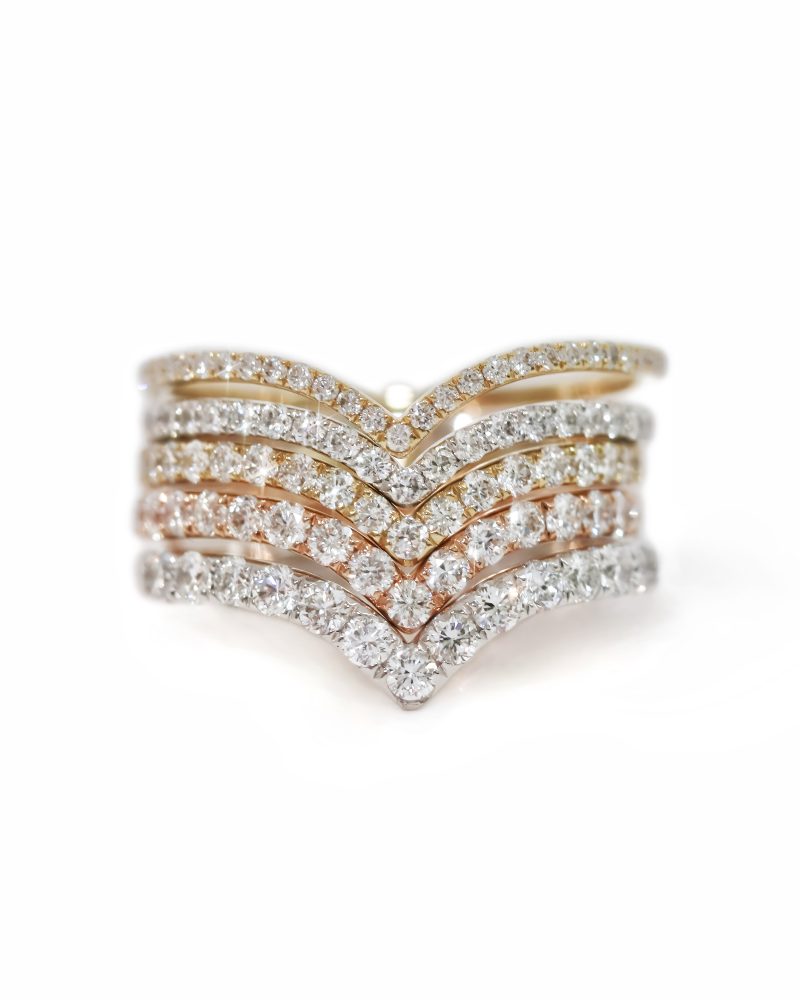 Five stacked V shape half enternity diamond rings in yellow, white, and rose gold on a white background. 黃金、白金與玫瑰金五戒疊戴特寫圖，展示V型排鑽戒指的搭配效果，純白背景。